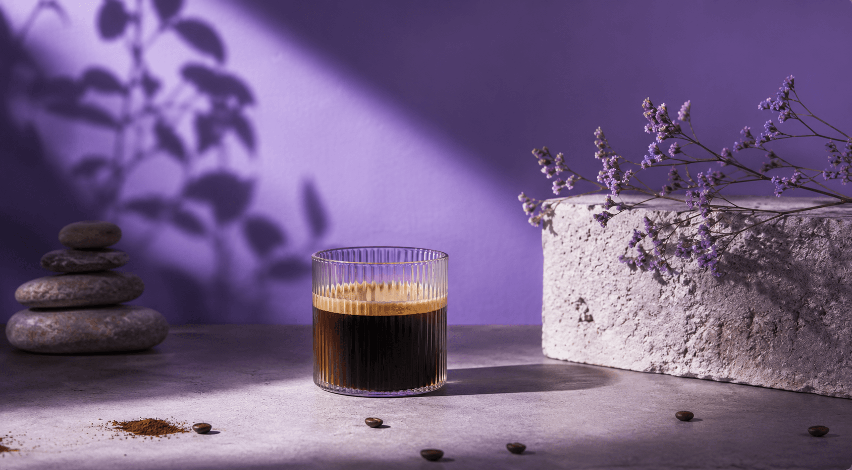 A glass of coffee in purple light with flowers and coffee beans